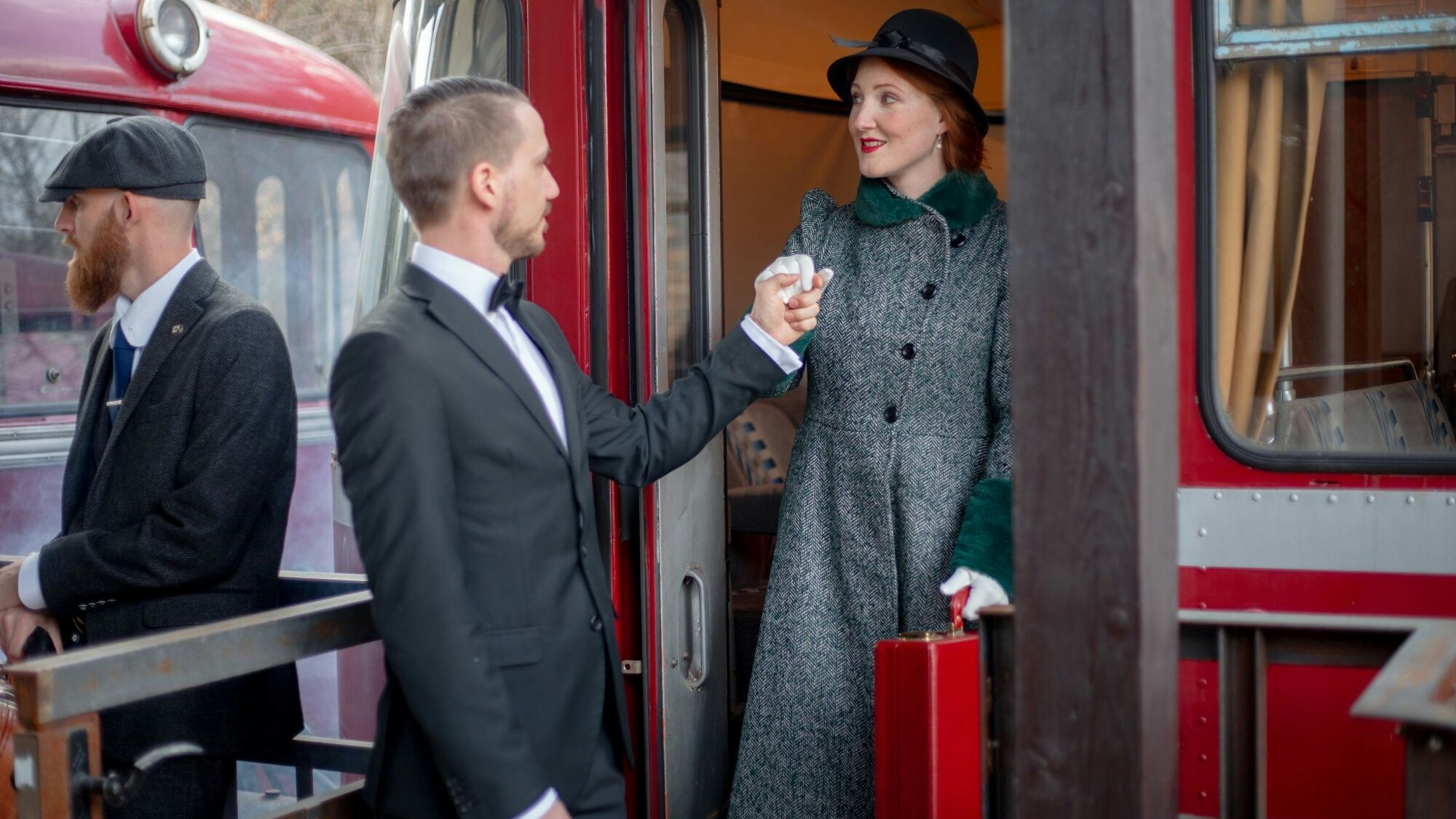 Darsteller in historischer Kleidung der 1920er-Jahre in einer Spielszene am Bahnsteig des Museumsbahnhofs mit einem roten Schienenbus im Hintergrund.