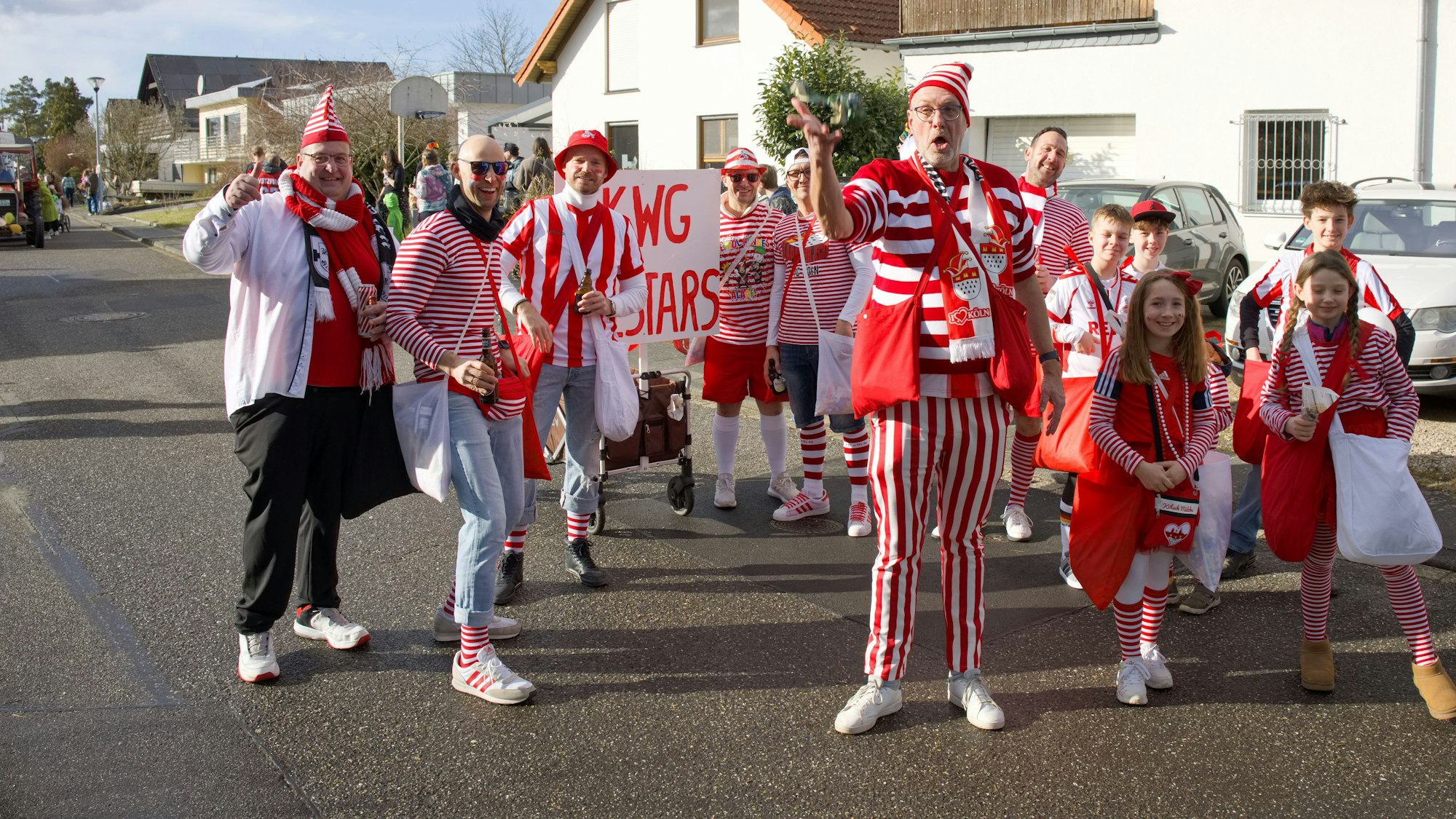 Eine Gruppe rot-weiß kostümierter Kinder und Erwachsener steht auf der Straße in einem Wohnviertel.