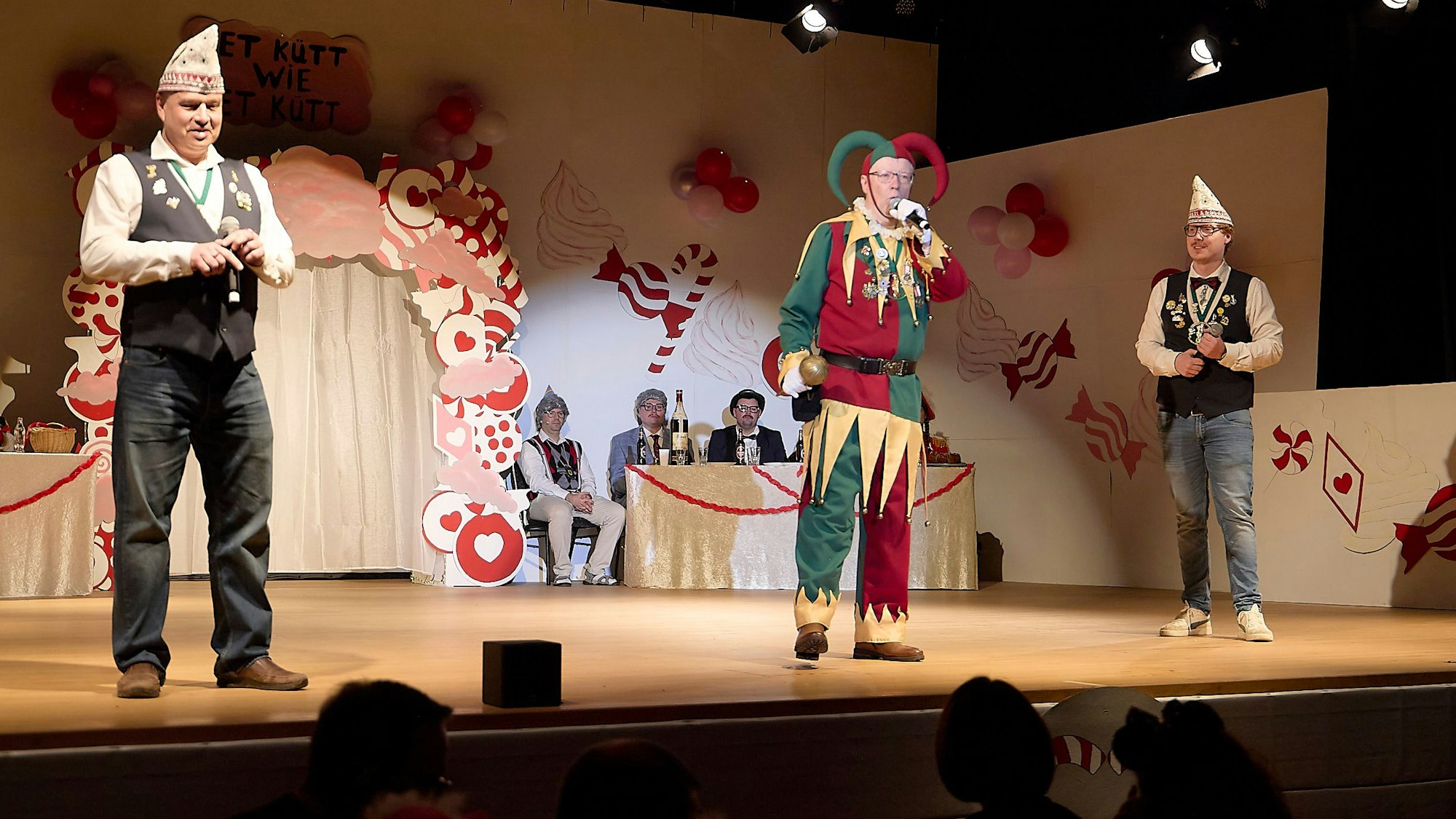 Bellejeck Dirk Gemünd, der ein Narrenkostüm trägt steht auf einer Bühne und singt in ein Mikrofon, dass er in der linken Hand hält.