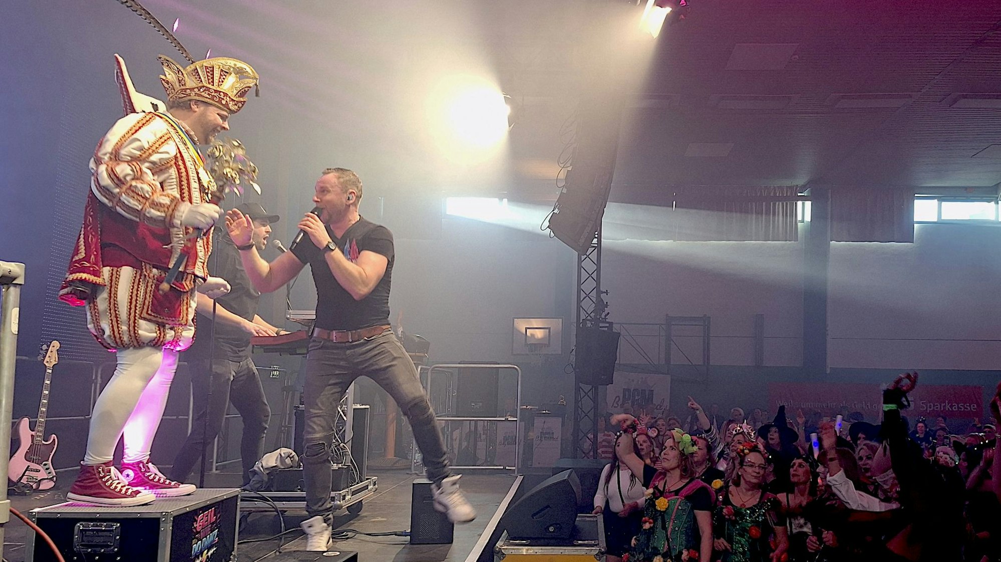 Der kostümierte Prinz Torsten I. steht neben dem Sänger Hubi Pieper auf einer Bühne vor Publikum.