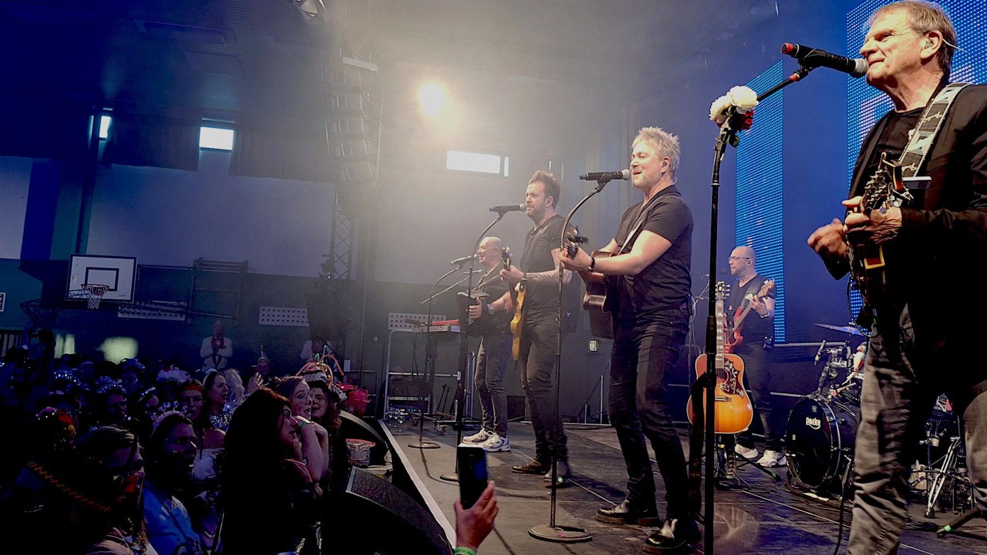 Die Musiker der Band Paveier spielen und singen auf einer angeleuchten Bühne.