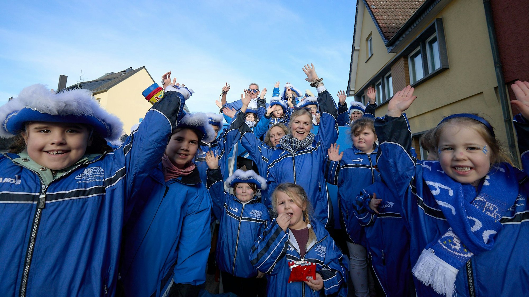 Kleine und große Karnevalisten der Blau-Weißen Schleidener heben ihre Hände in die Luft. Ein Mädchen isst derweil aus einer Tüte.