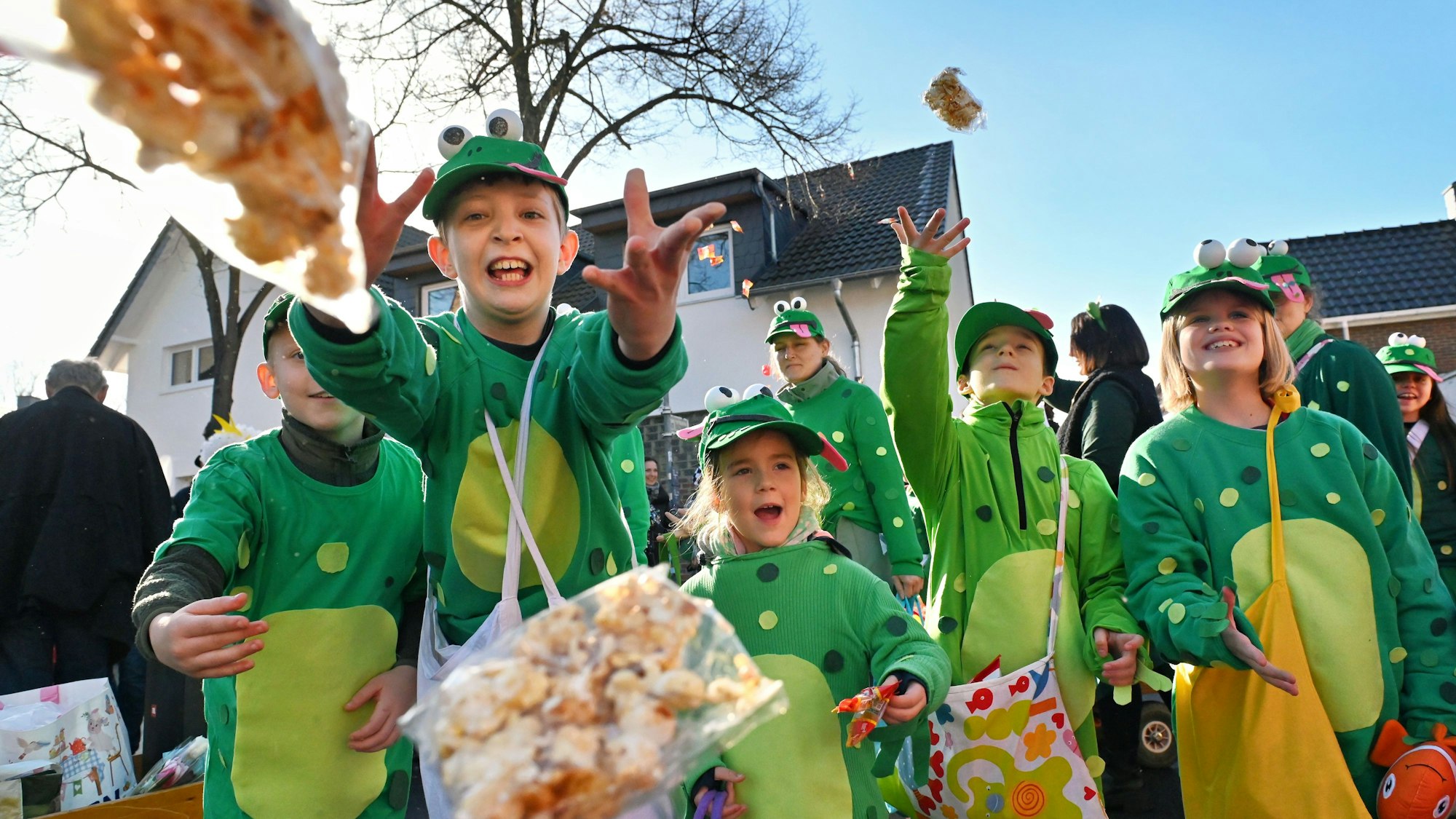 Kinder, die als Frösche verkleidet sind, werfen Kamella auf einem Karnevalszug.