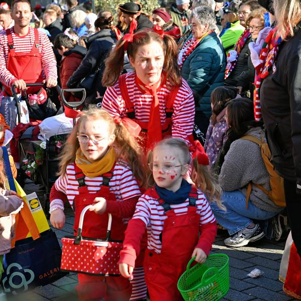 Eine Familie in gestreiften Karnevalskostümen bahnt sich ihren Weg durch die Zuschauer des Kinderzugs in Euskirchen.