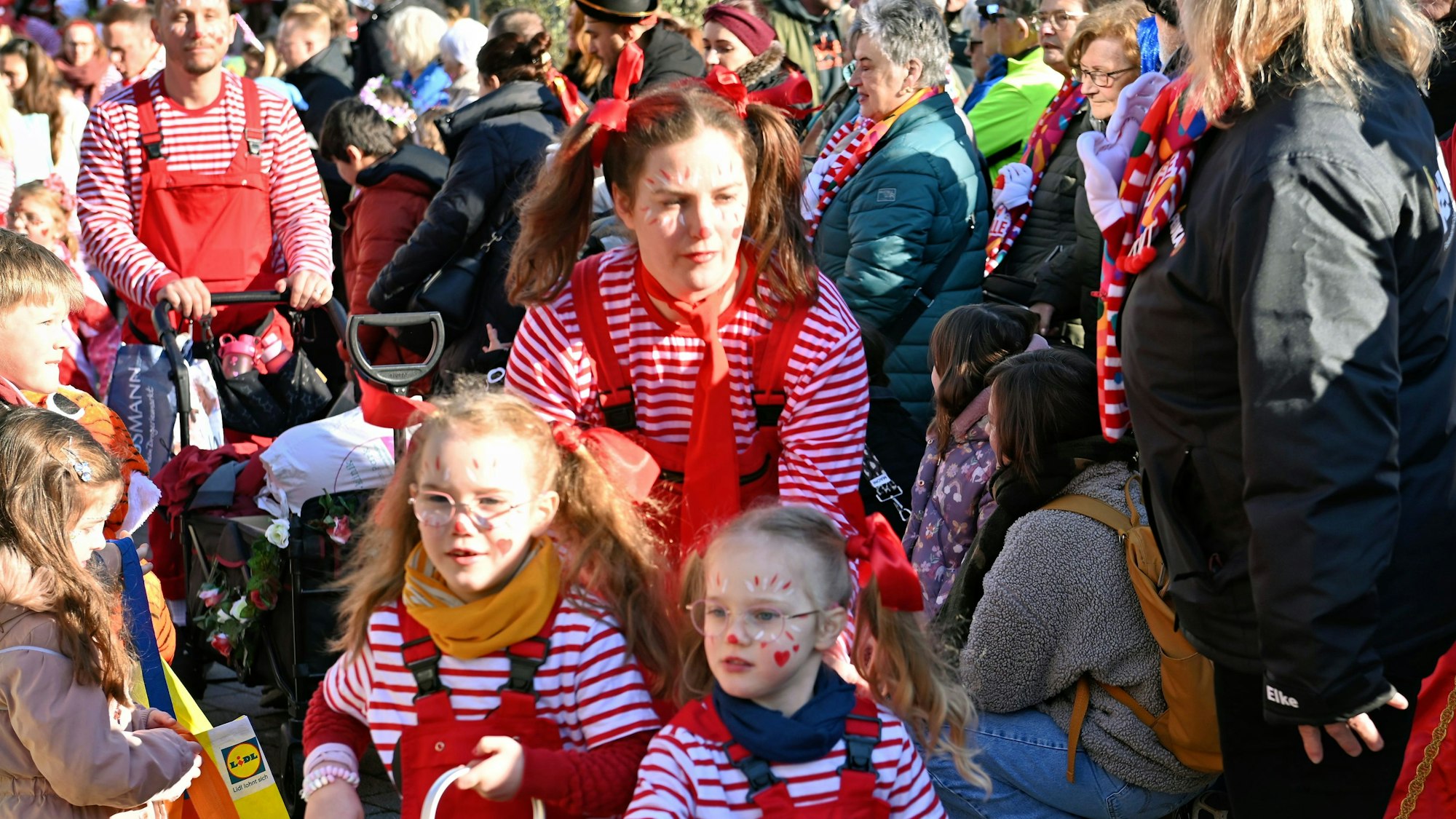Eine Familie in gestreiften Karnevalskostümen bahnt sich ihren Weg durch die Zuschauer des Kinderzugs in Euskirchen.