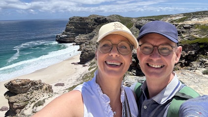 Das Foto zeigt das Ehepaar vor einer malerischen Küstenlandschaft.