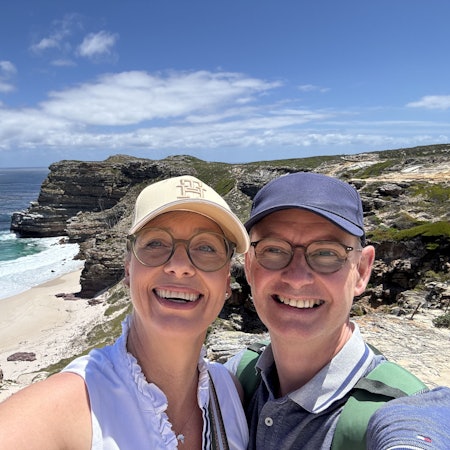 Das Foto zeigt das Ehepaar vor einer malerischen Küstenlandschaft.