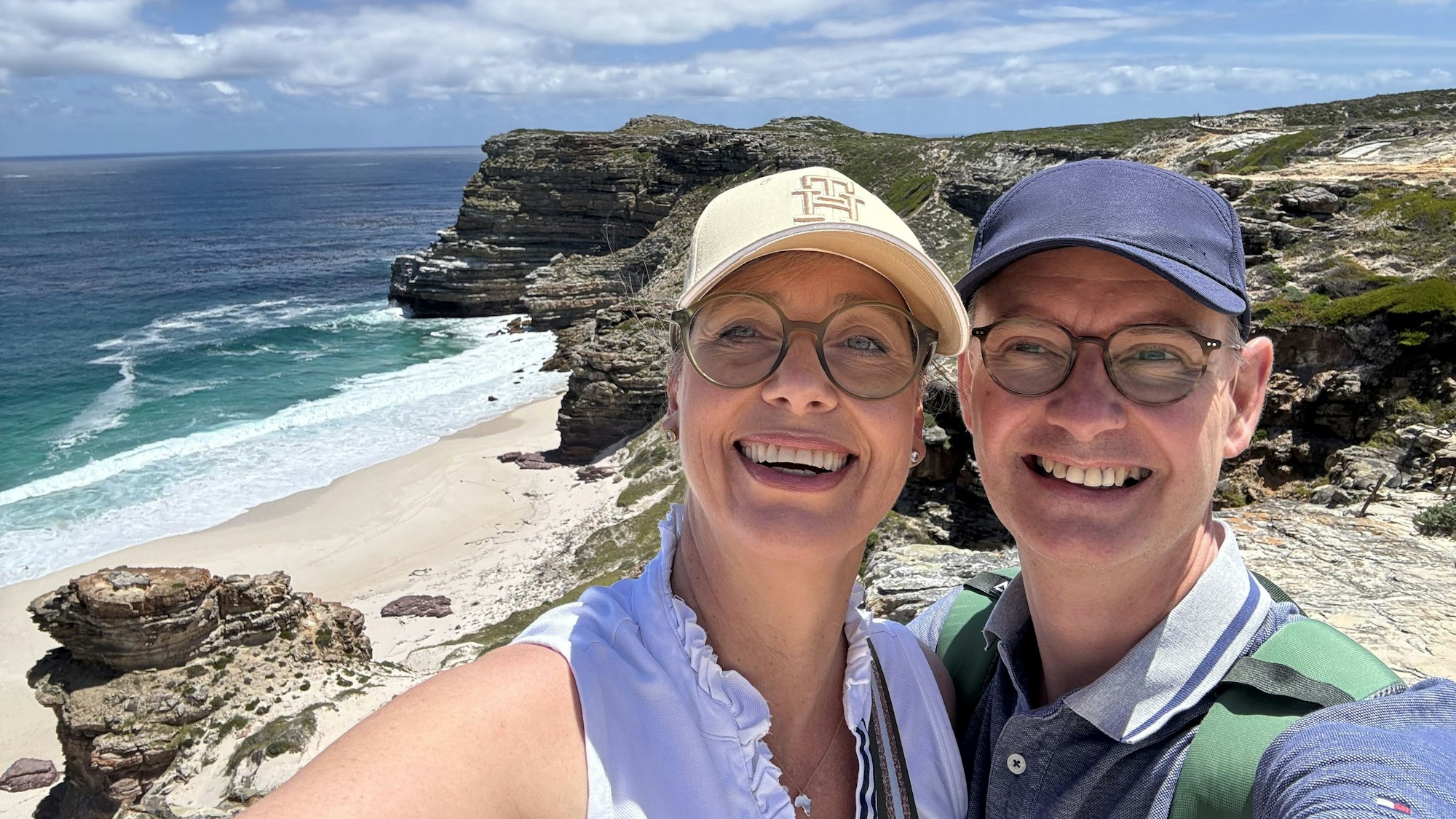 Das Foto zeigt das Ehepaar vor einer malerischen Küstenlandschaft.