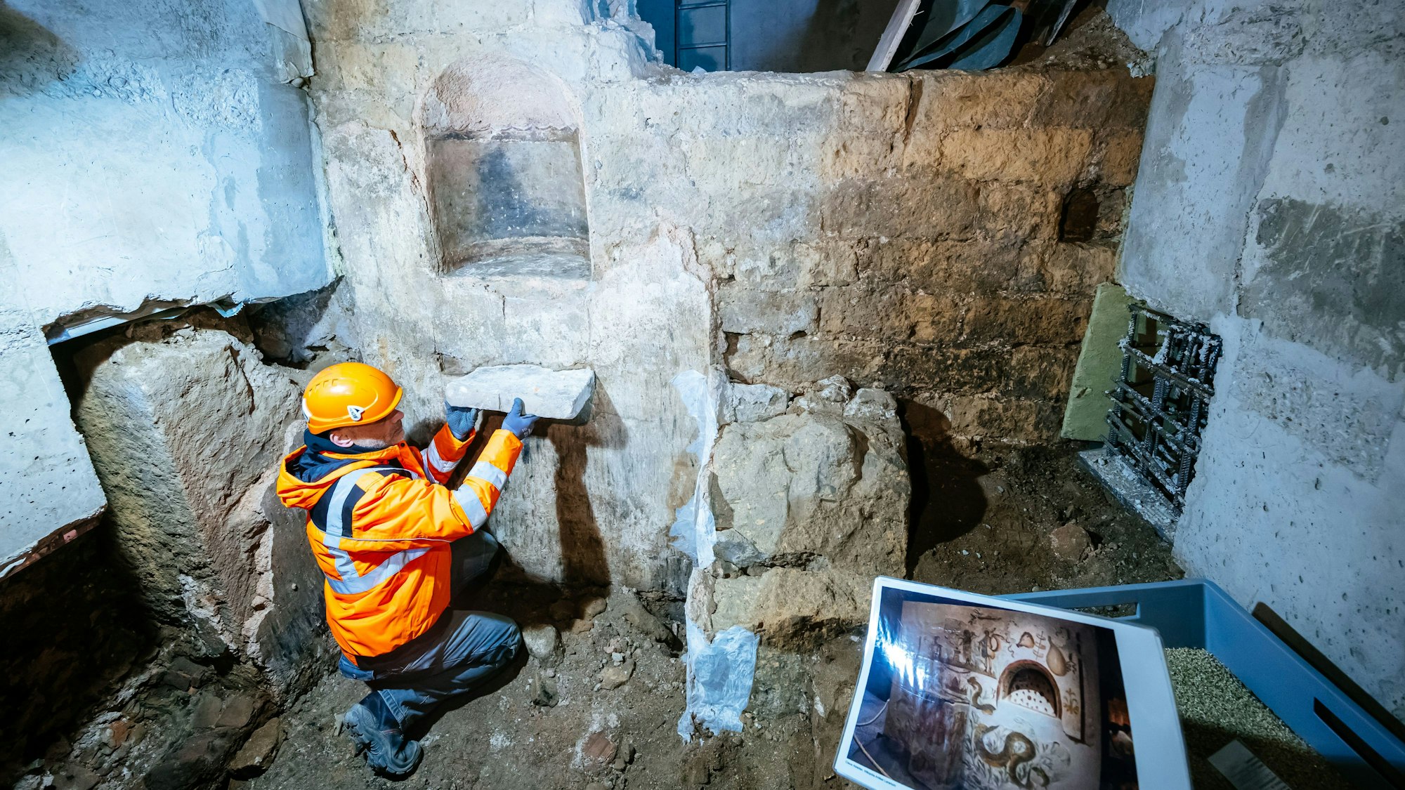 Ein Mann kniet vor einem steinernen Altar auf der MiQua-Baustelle in Köln.