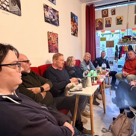 In den Räumen von Simons Glück sitzen die Teilnehmenden. Vor sich auf den Tischen stehen Getränke.