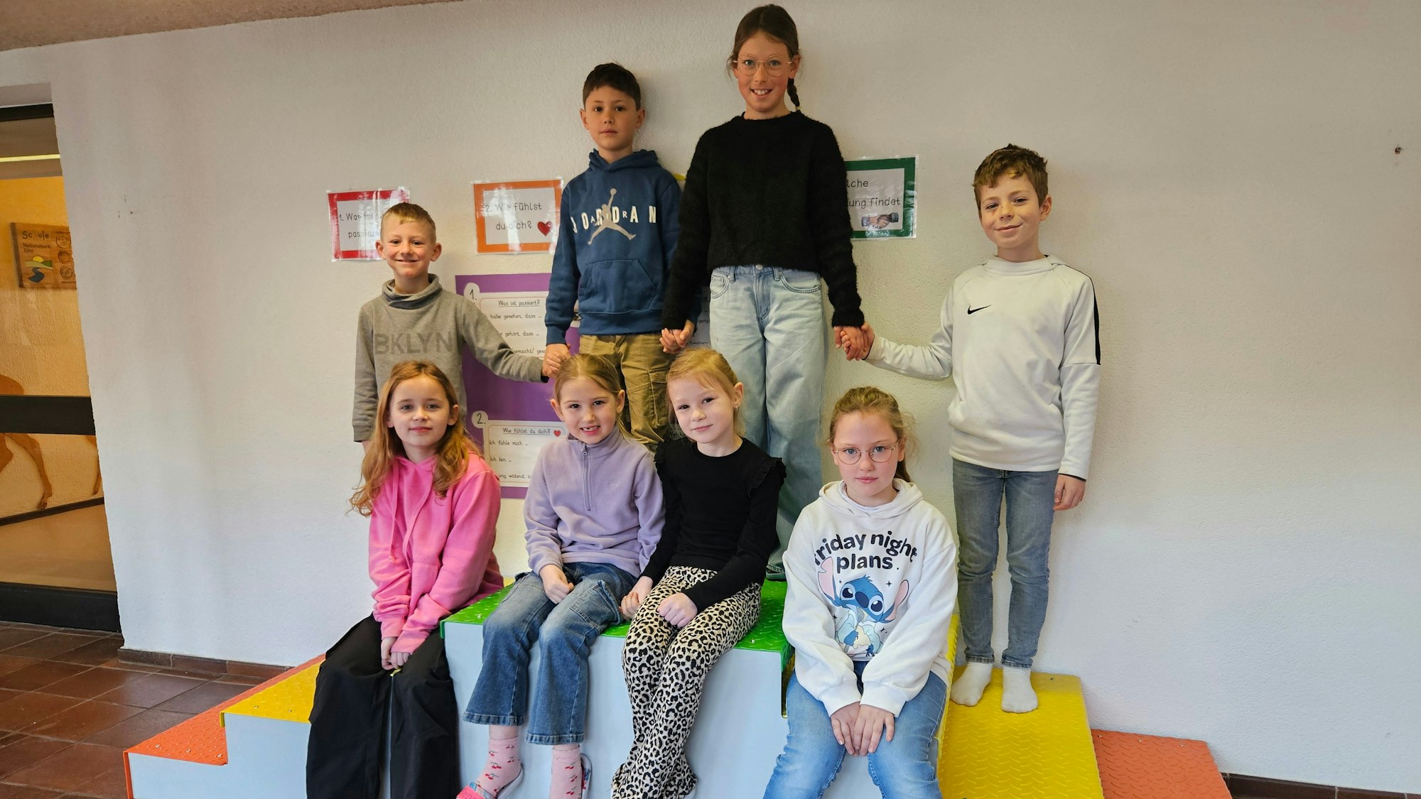 Kinder sitzen und stehen auf der Treppe mit verschiedenfarbigen Stufen.