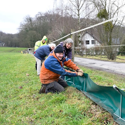 Vier Menschen stecken auf einer Wiese einen grünen Folienzaun in Metallbügel.