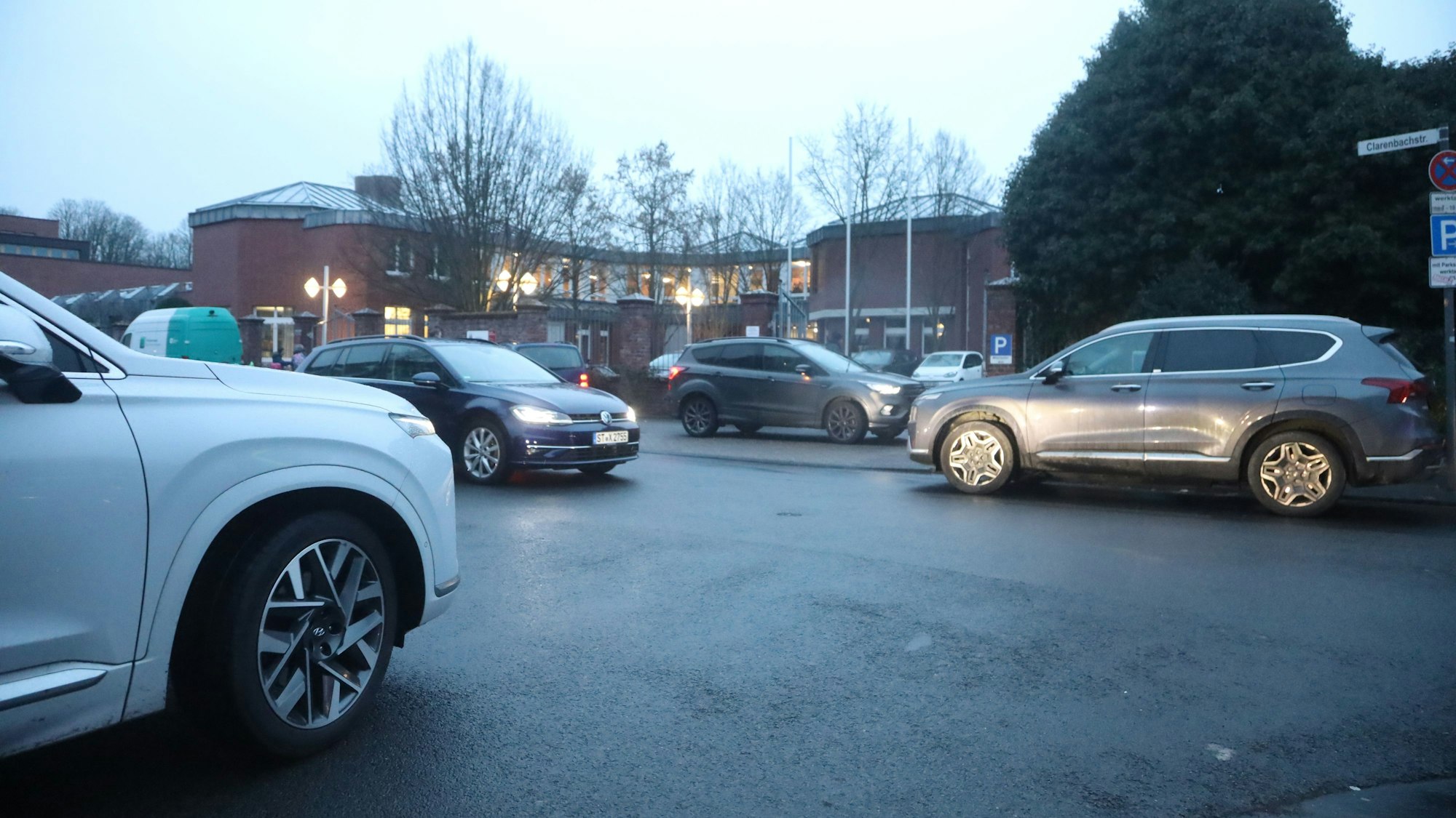 Mehrere Autos parken vor einem Schulgebäude oder fahren auf dieses zu.