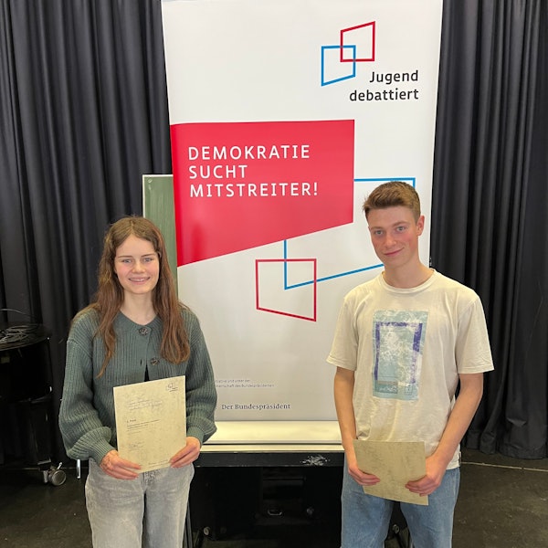 Eine Jugendliche und ein Jugenlicher schauen in die Kamera.