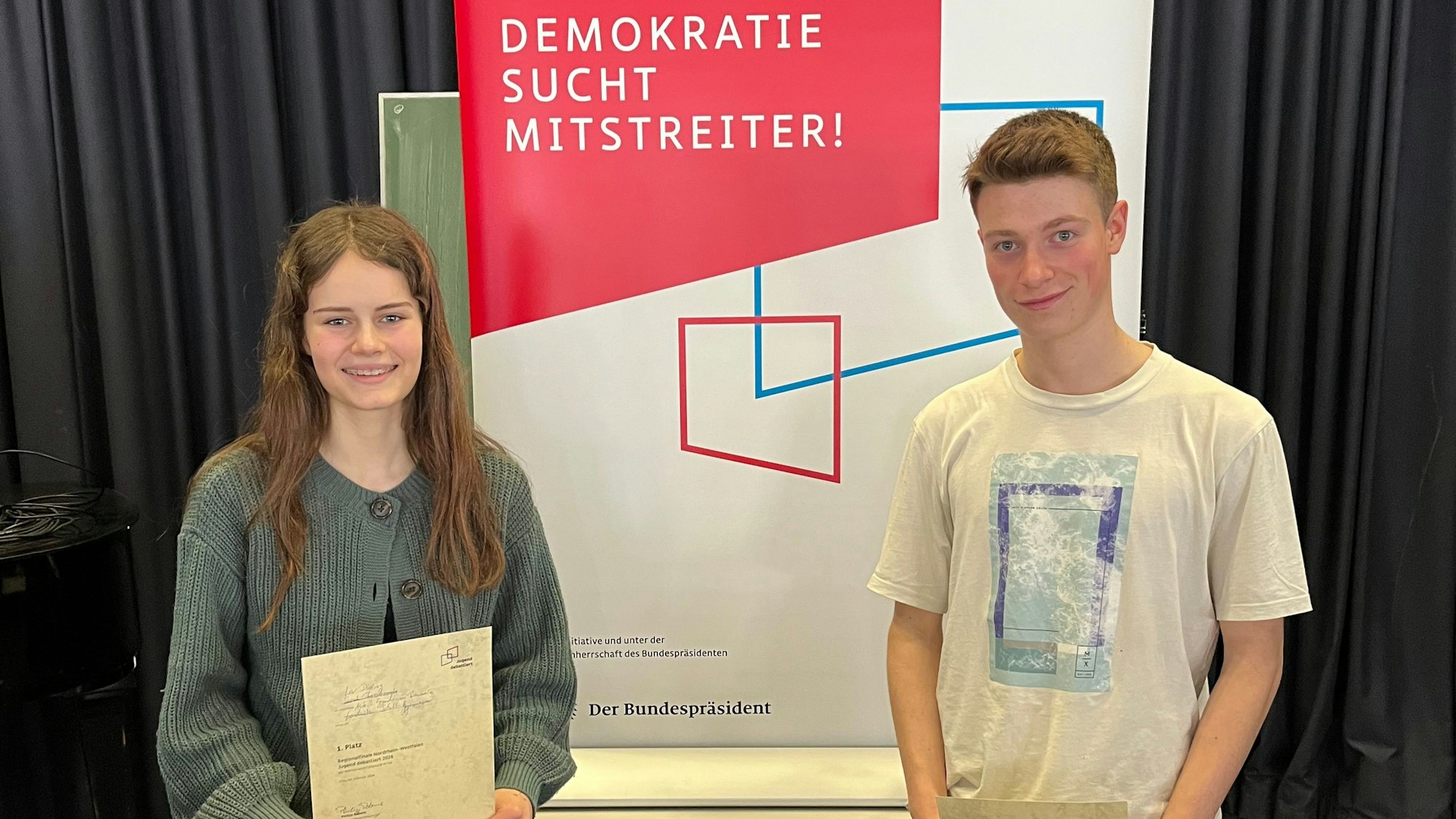 Eine Jugendliche und ein Jugenlicher schauen in die Kamera.