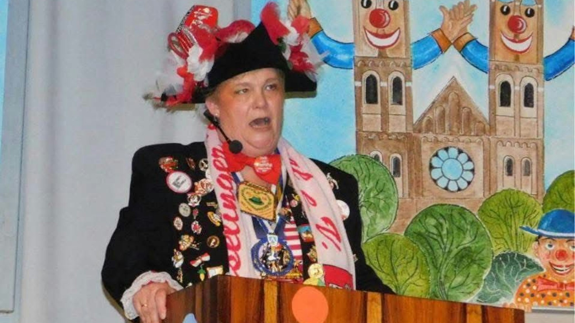 Eine Frau, im Karnevalsoutfit, steht an einem Rednerpult.