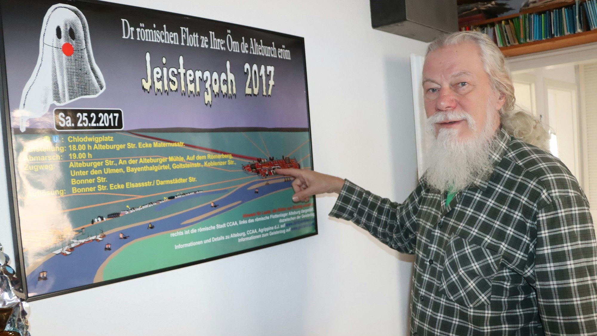 Ein Mann mit langen weißen Haaren und einem langen weißen Bart zeigt auf ein Mottobild des Geisterzugs.