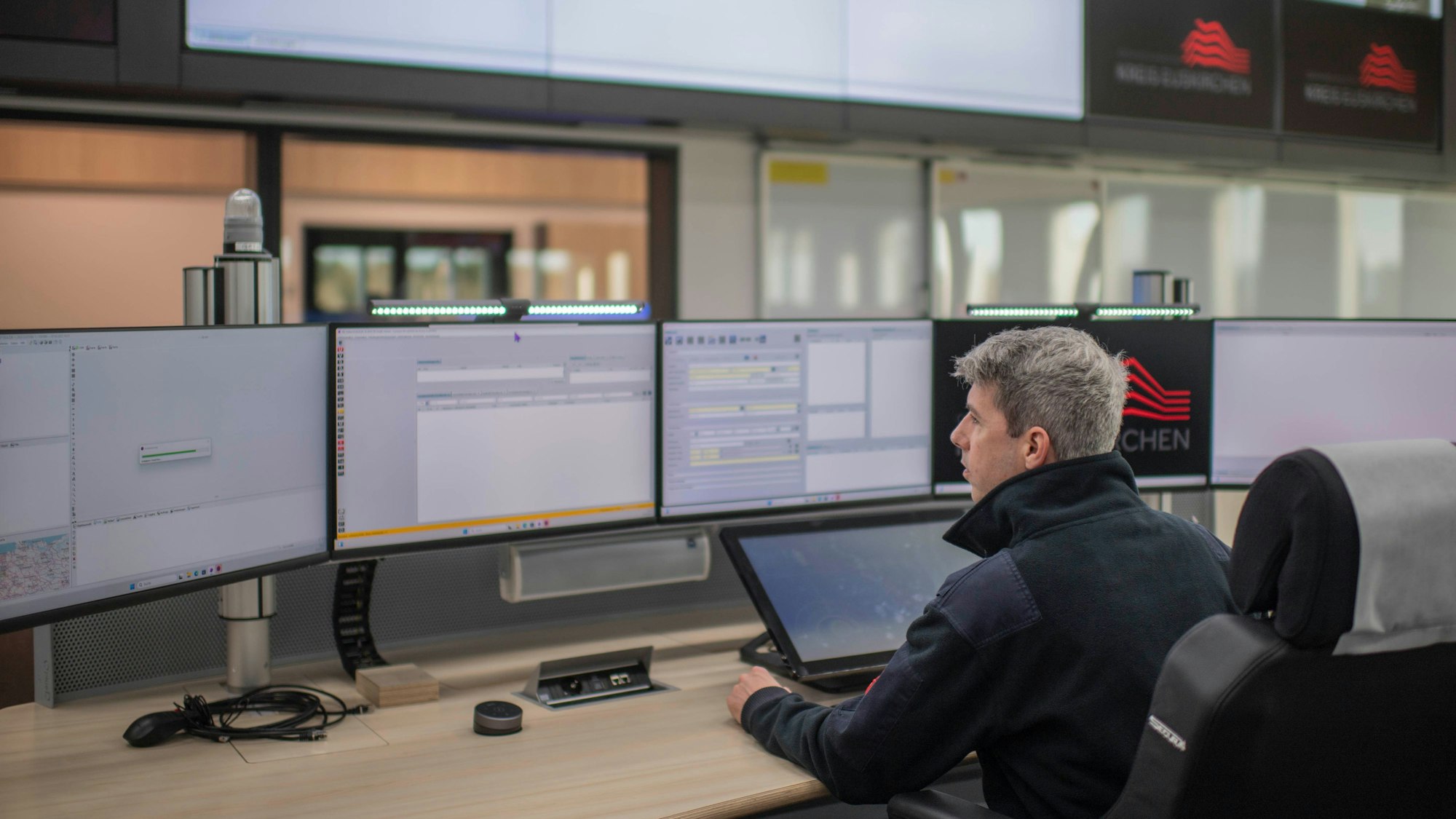 Ein Mann sitzt vor einer Reihe von Bildschirmen.