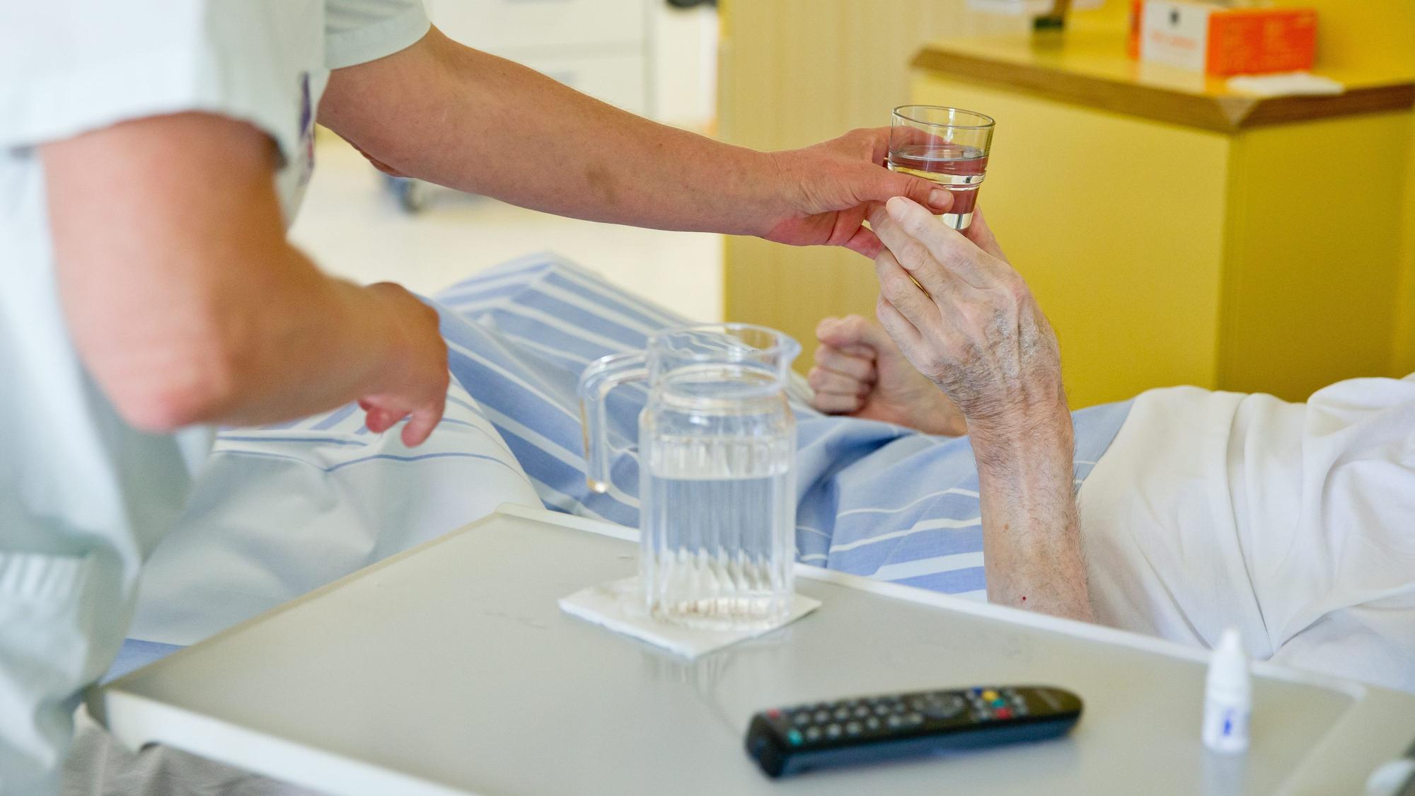 Eine Krankenpflegerin reicht einem Patienten in einem Klinikum ein Glas Wasser. (Symbolbild)