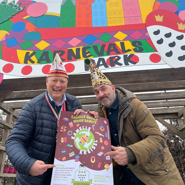 Das Foto zeigt den Landwirt und den Karnvalisten mit Karnevalsmützen und Plakat vor dem Karnevalspark auf dem Gertrudenhof.