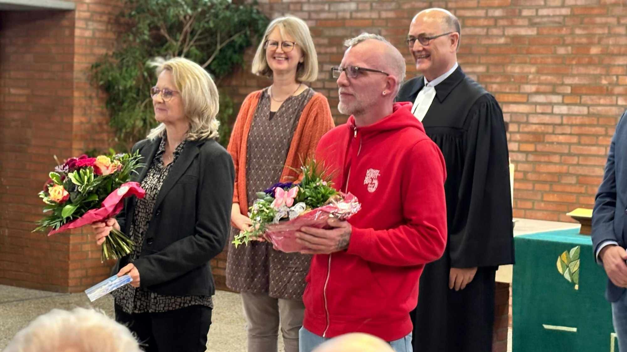 Ein Mann und eine Frau halten Blumensträuße in den Händen und schauen auf etwas außerhalb des Bildausschnitts.