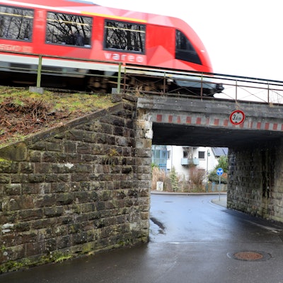 Eine rote Regionalbahn fährt über eine Brücke mit einem schmalen Durchgang.