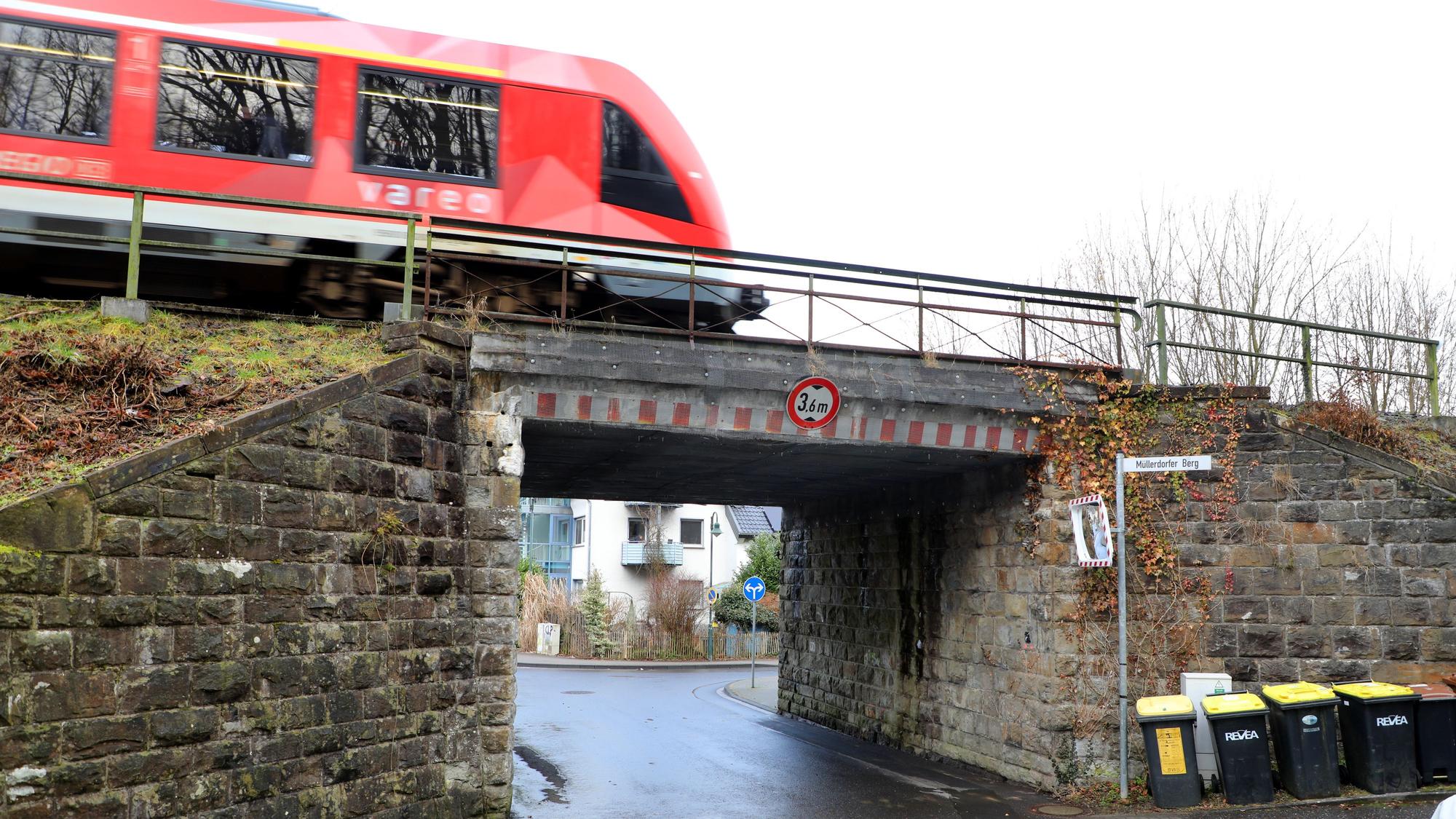 Eine rote Regionalbahn fährt über eine Brücke mit einem schmalen Durchgang.