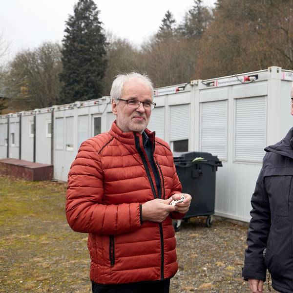 Das Bild zeigt die Obengenannten. Im Hintergrund sind Wohncontainer zu sehen.