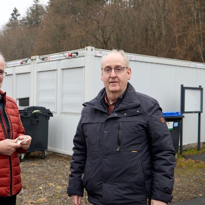 Das Bild zeigt die Obengenannten. Im Hintergrund sind Wohncontainer zu sehen.