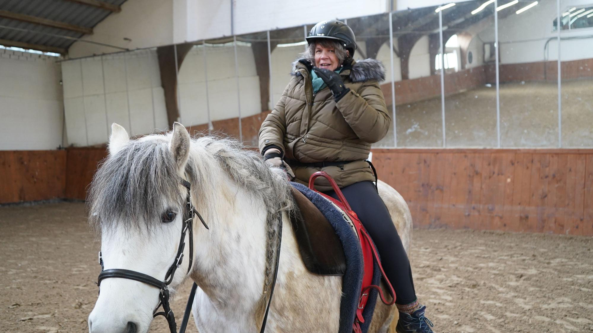 Das Bild zeigt die Reiterin auf einem weißen Pferd.