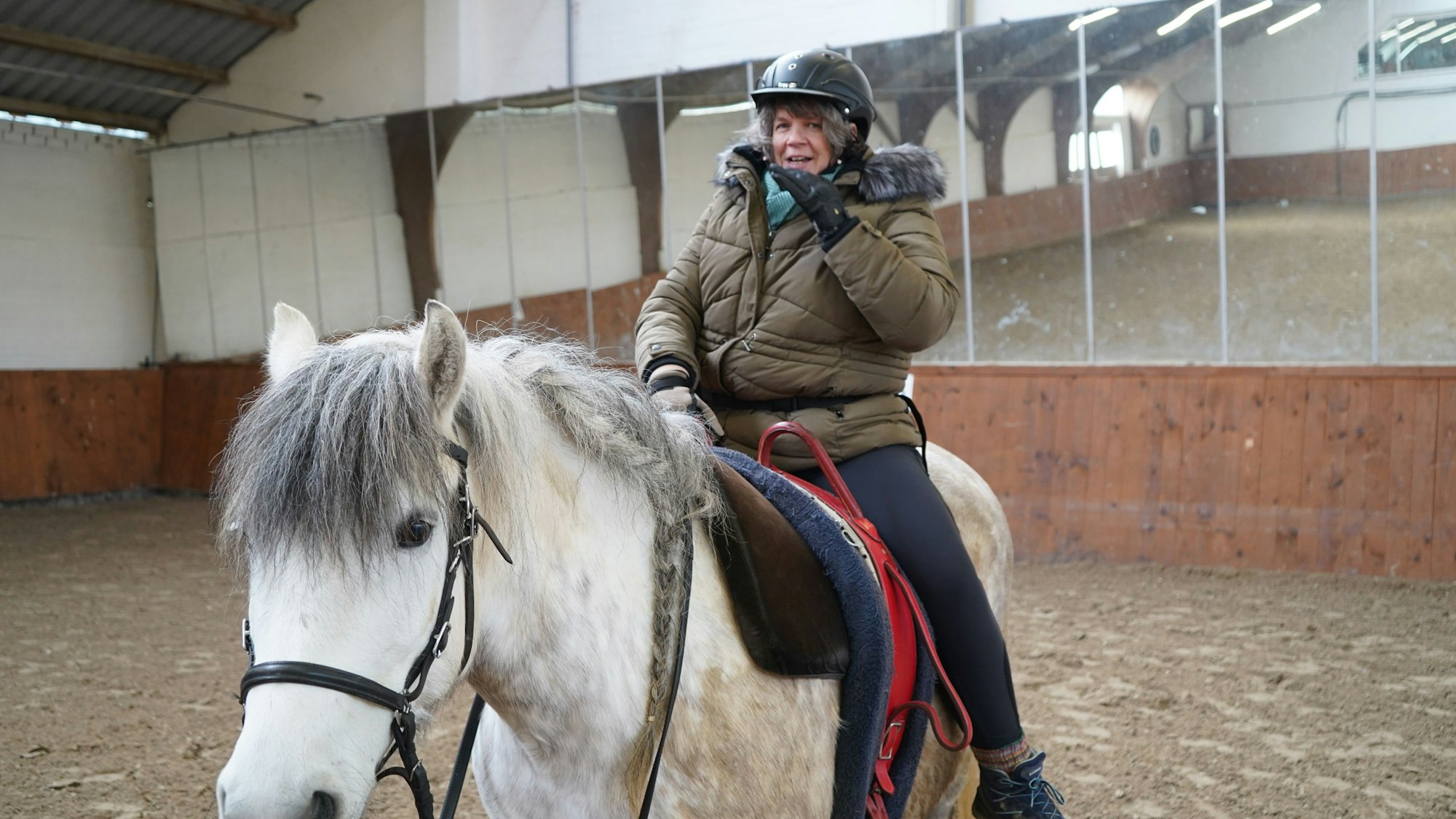 Das Bild zeigt die Reiterin auf einem weißen Pferd.