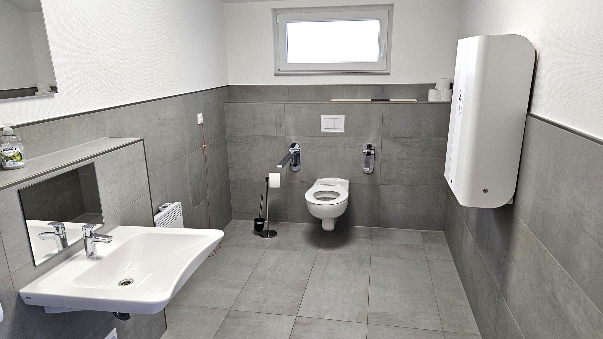 Blick in die Sanitäranlage für Menschen mit Behinderung. Rechts an der Wand hängt ein Wickeltisch.