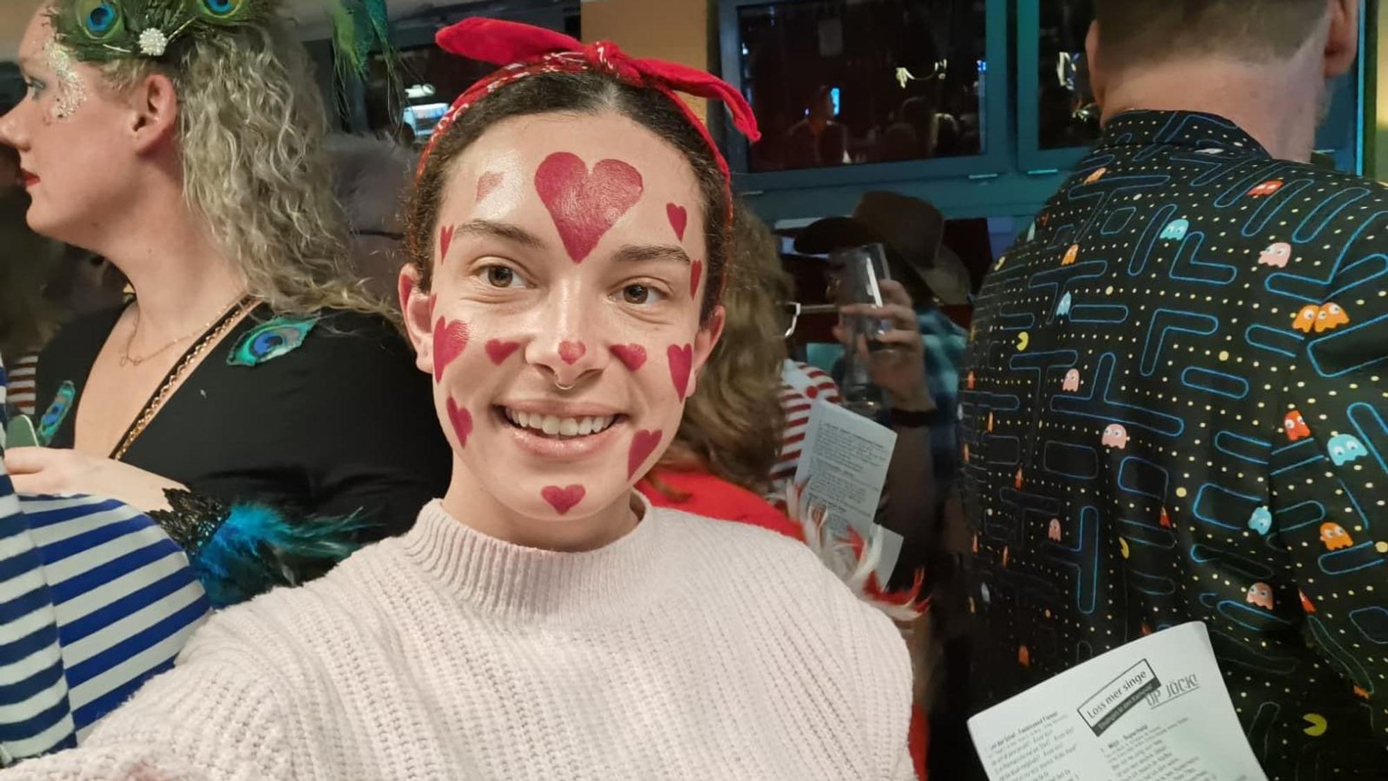 Eine Frau mit Herzen ins Gesicht gemalt lächelt in die Kamera.