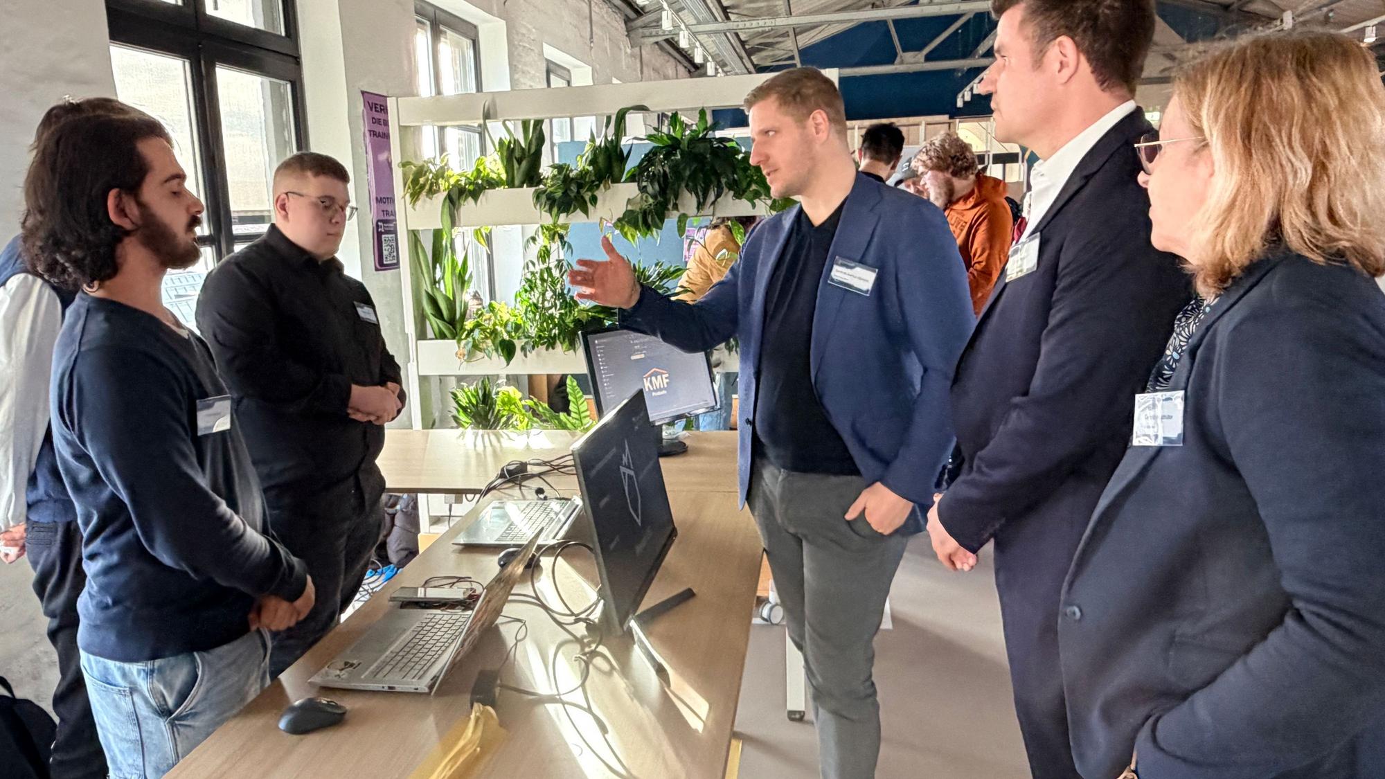 Drei Schüler stehen an ihrem Stand, auf dem Tisch vor sich Computer. Sie sind im Gespräch mit Landrat Markus Ramers,TEB-Bereichsleiter David Breuer und Schulleiterin Carolin Holzhüter.