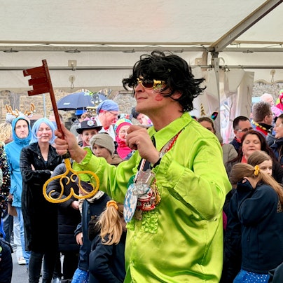 Bürgermeister Sebastian Glatzel im grellgrünen Hemd und mit schwarzer Perücke dirigiert mit dem Stadtschlüssel in der Hand.