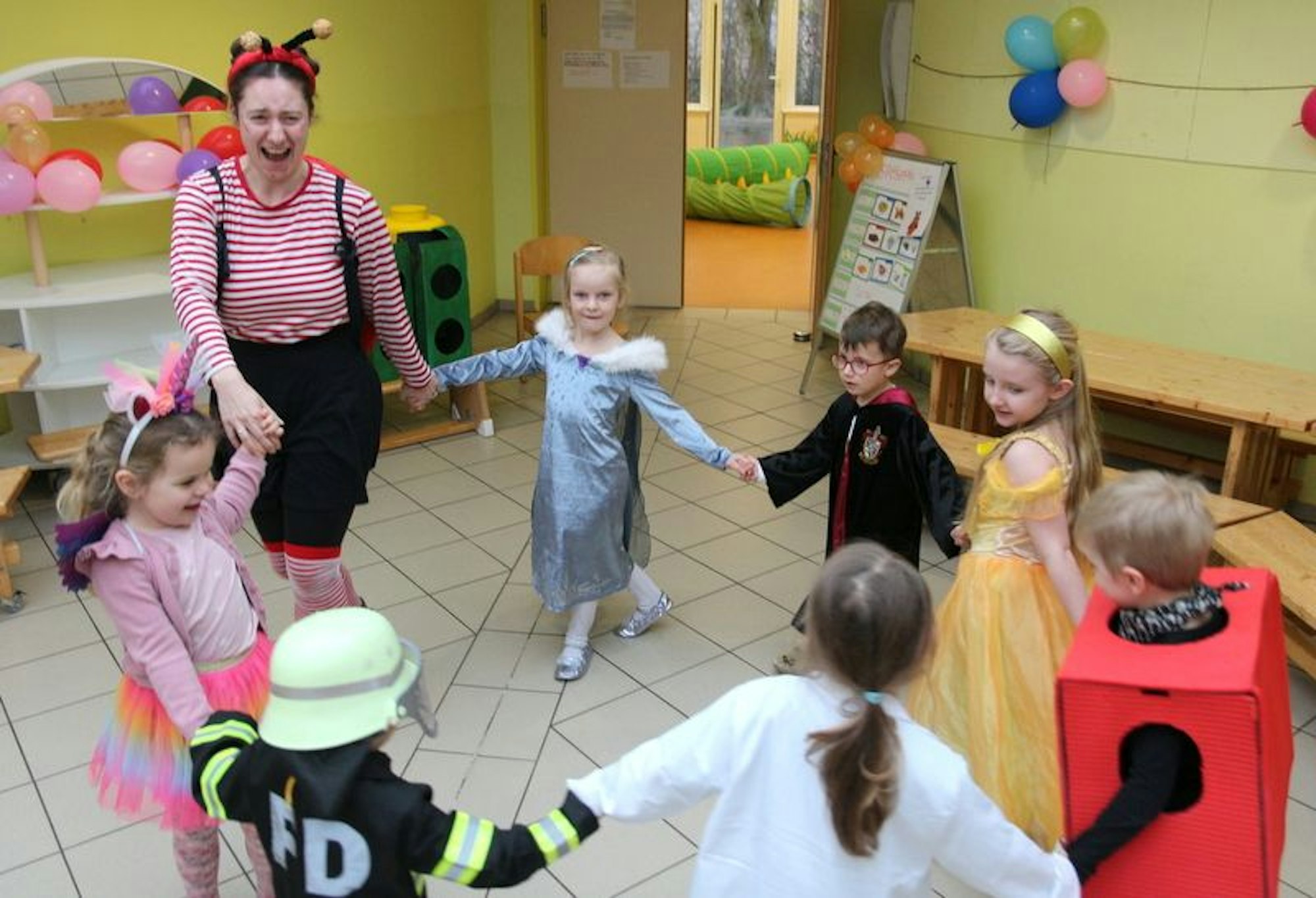 Auf dem Bild sind kostümierte Kinder zu sehen, die in einem Kreis tanzen.