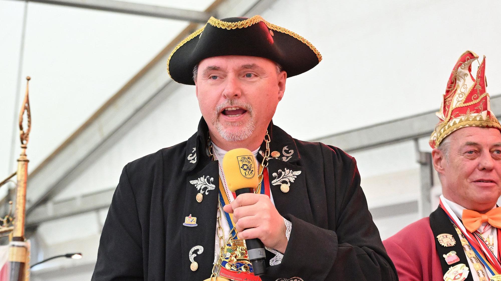 Michael Eyer spricht in ein Mikrofon und trägt einen schwarzen Hut mit goldener Krempe.