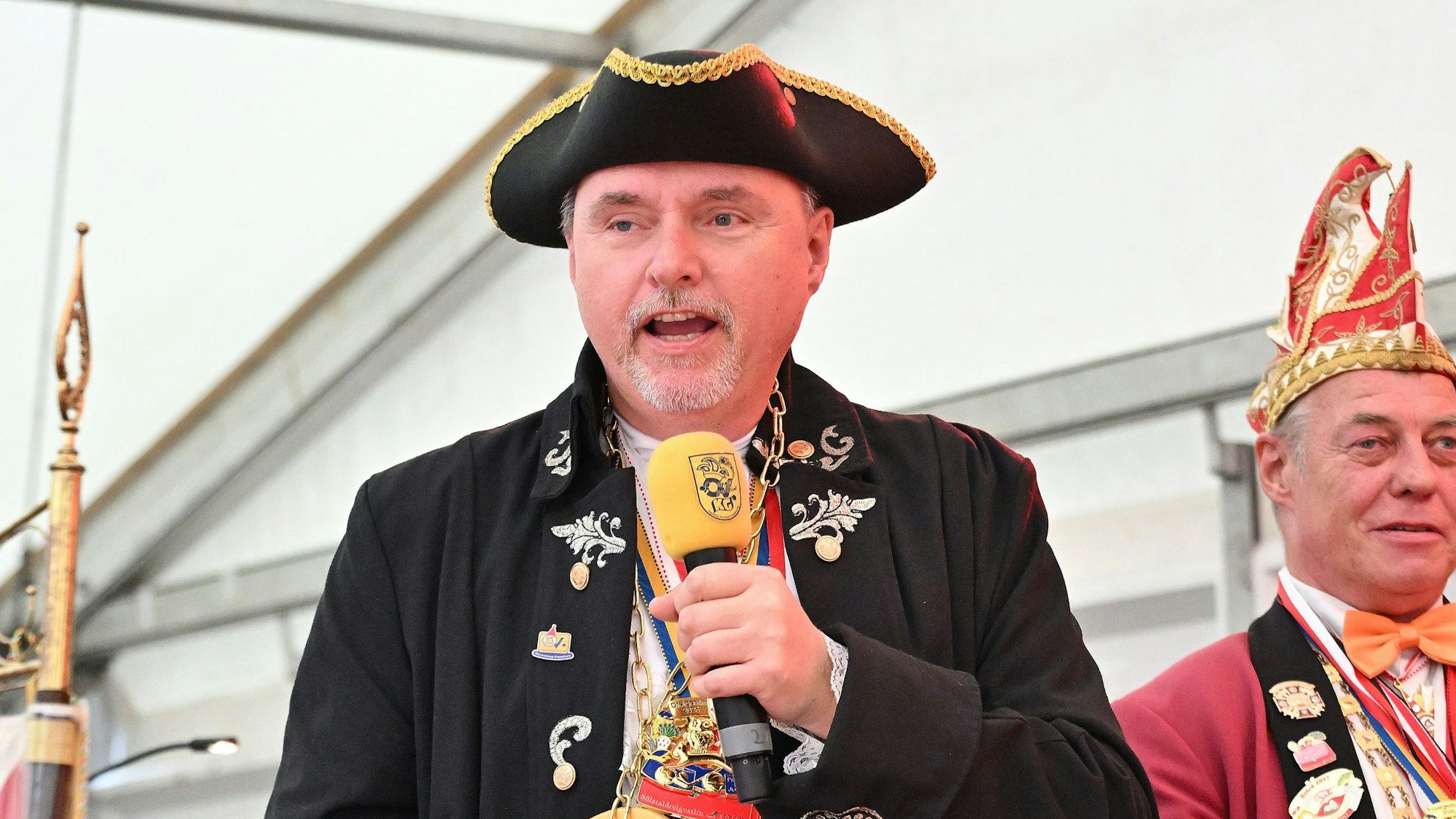 Michael Eyer spricht in ein Mikrofon und trägt einen schwarzen Hut mit goldener Krempe.