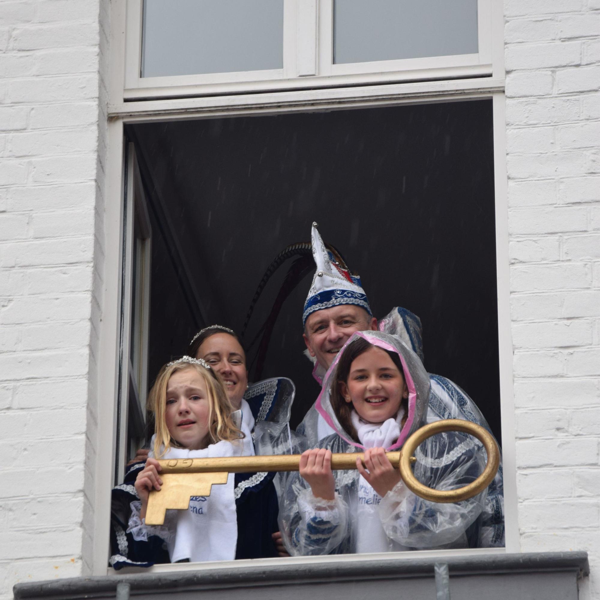 Zwei Kinderprinzessinnen und ein Prinzenpaar in blau-weißem Ornat schauen aus einem Fenster. In der Hand haben sie einen großen goldenen Schlüssel.
