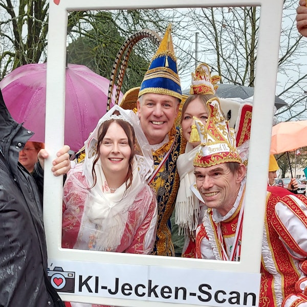 Zwei Karnevalsprinzen im Ornat und zwei Prinzessinnen schauen durch einen Bilderrahmen.