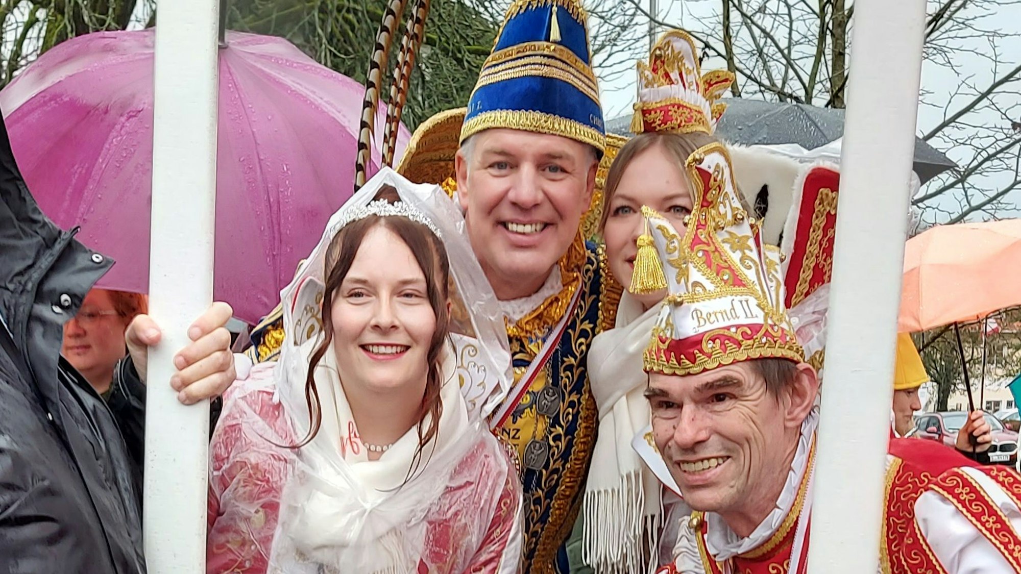 Zwei Karnevalsprinzen im Ornat und zwei Prinzessinnen schauen durch einen Bilderrahmen.