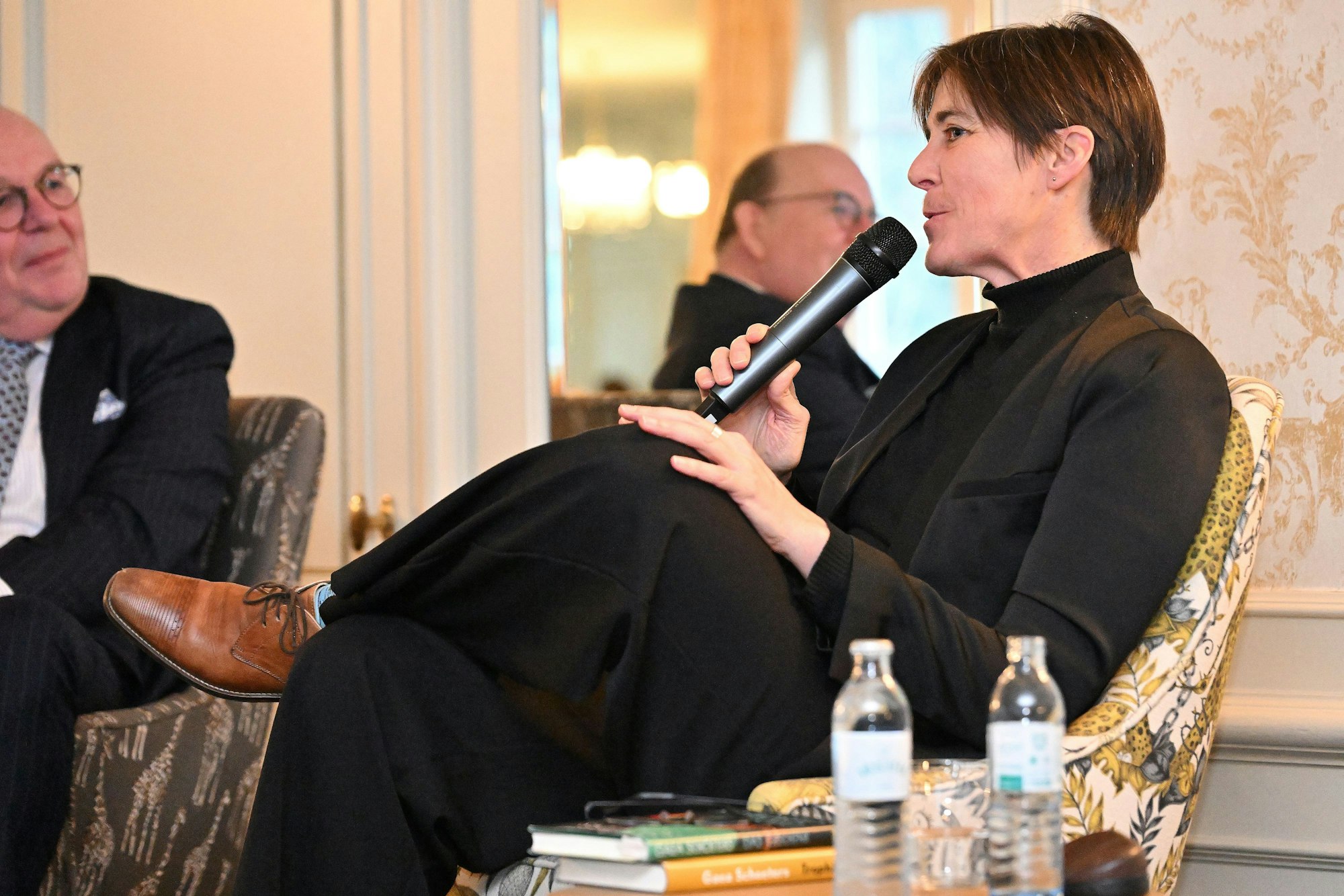 Links sitzt Denis Scheck. Er hört der neben ihm sitzenden, schwarz gekleideten Autorin Gaea Schoeters zu, die in ein Mikro spricht.