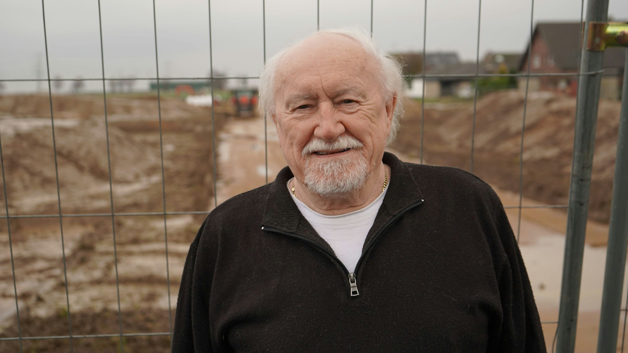 Das Bild zeigt den Angehörigen vor einem Bauzaun, dahinter die Baustellen.