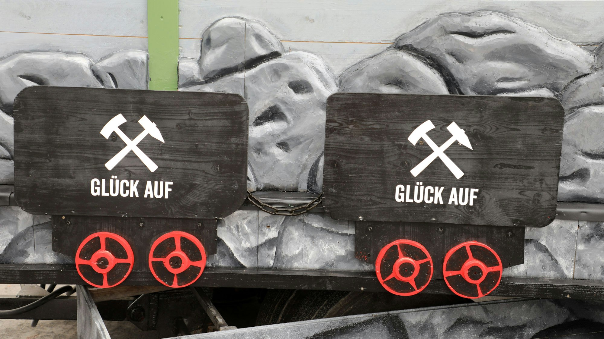 Zwei schwarze Loren, Förderwagen, in denen Erz transportiert wurde, mit Bergbau-Logo und je zwei roten Rädern wurden am unteren Teil des Wagens nachgebildet.