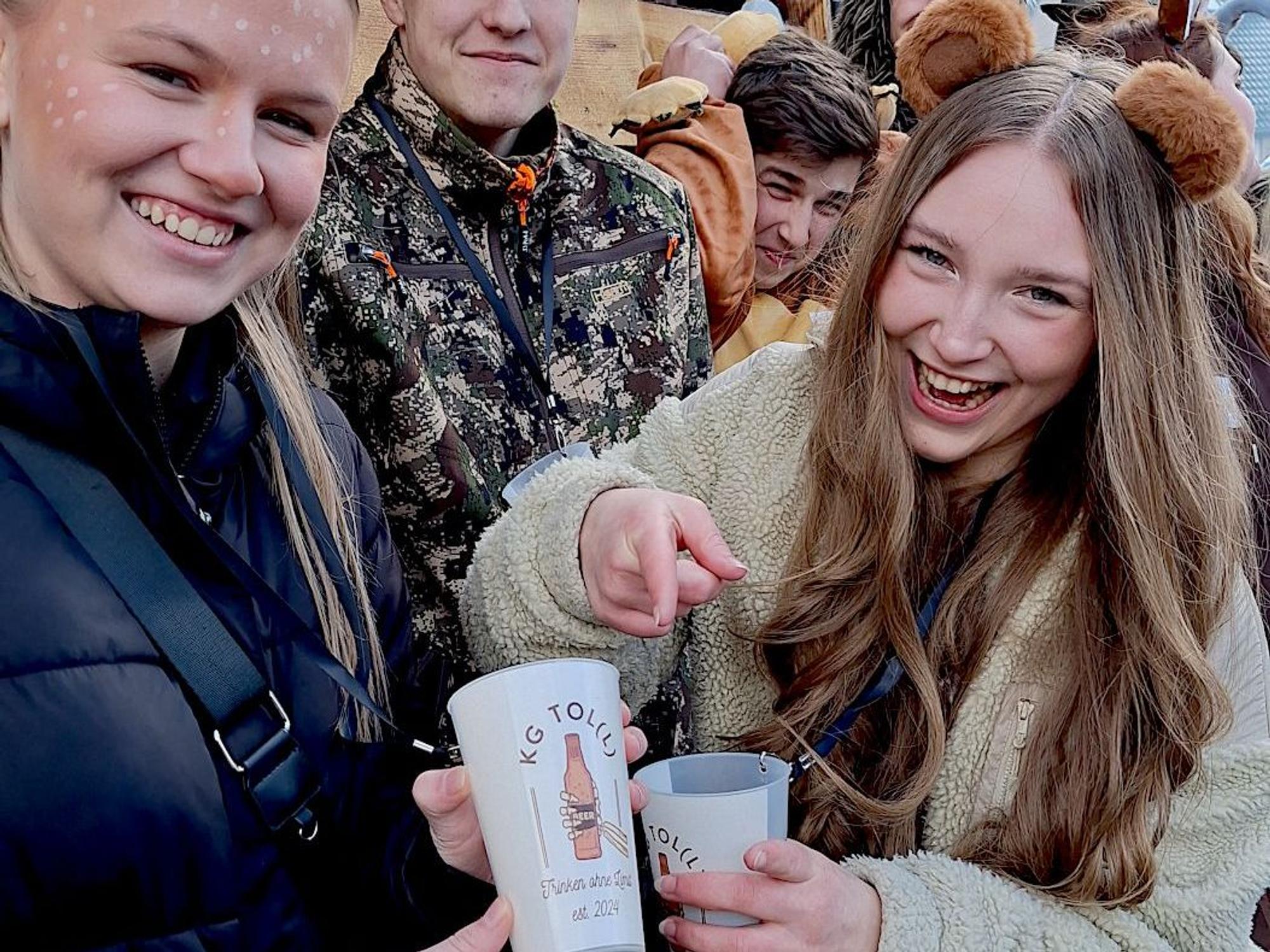 Eine junge Frau zeigt auf einen Trinkbecher, den eine andere Frau in der Hand hält.
