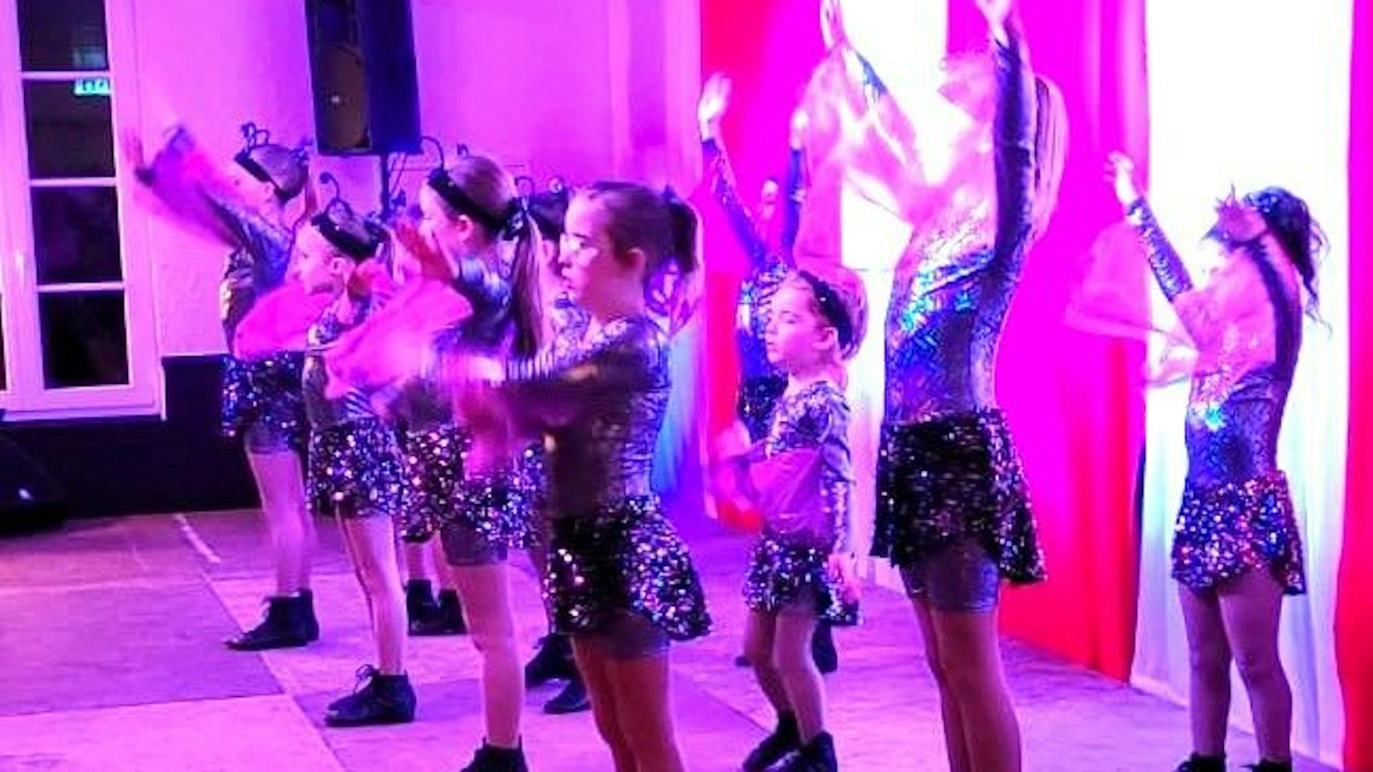 Das Bild zeigt eine Kindertanzgruppe, die in rosa Bühnenlicht getaucht sind.