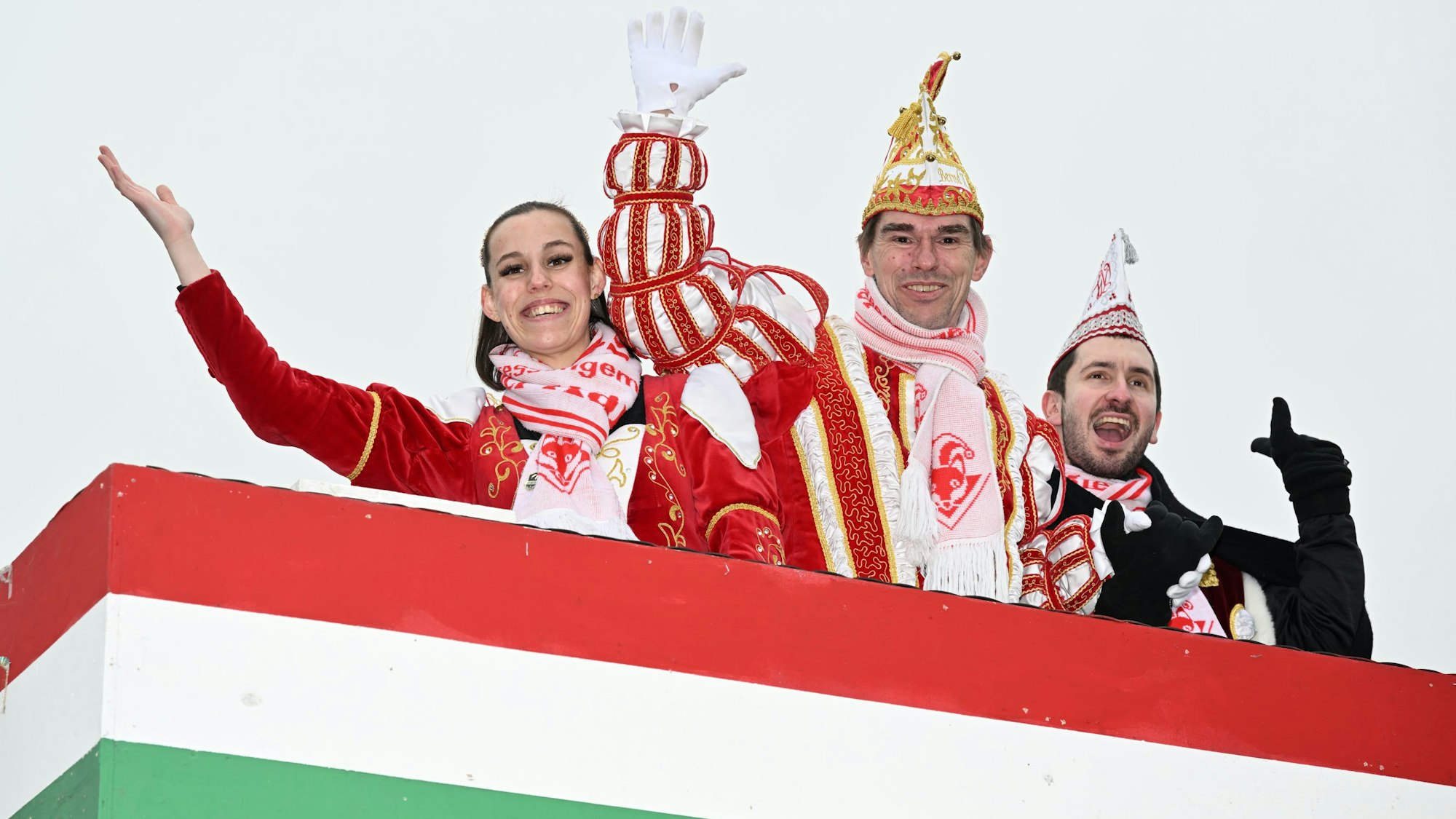 Ein Dreigestirn mit Prinz, Jungfrau und Bauer in rot-weißem Ornat winken von einem Festwagen.