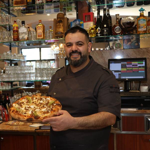 Auf dem Bild ist ein Mann mit einer frisch gebackenen Pizza zu sehen.