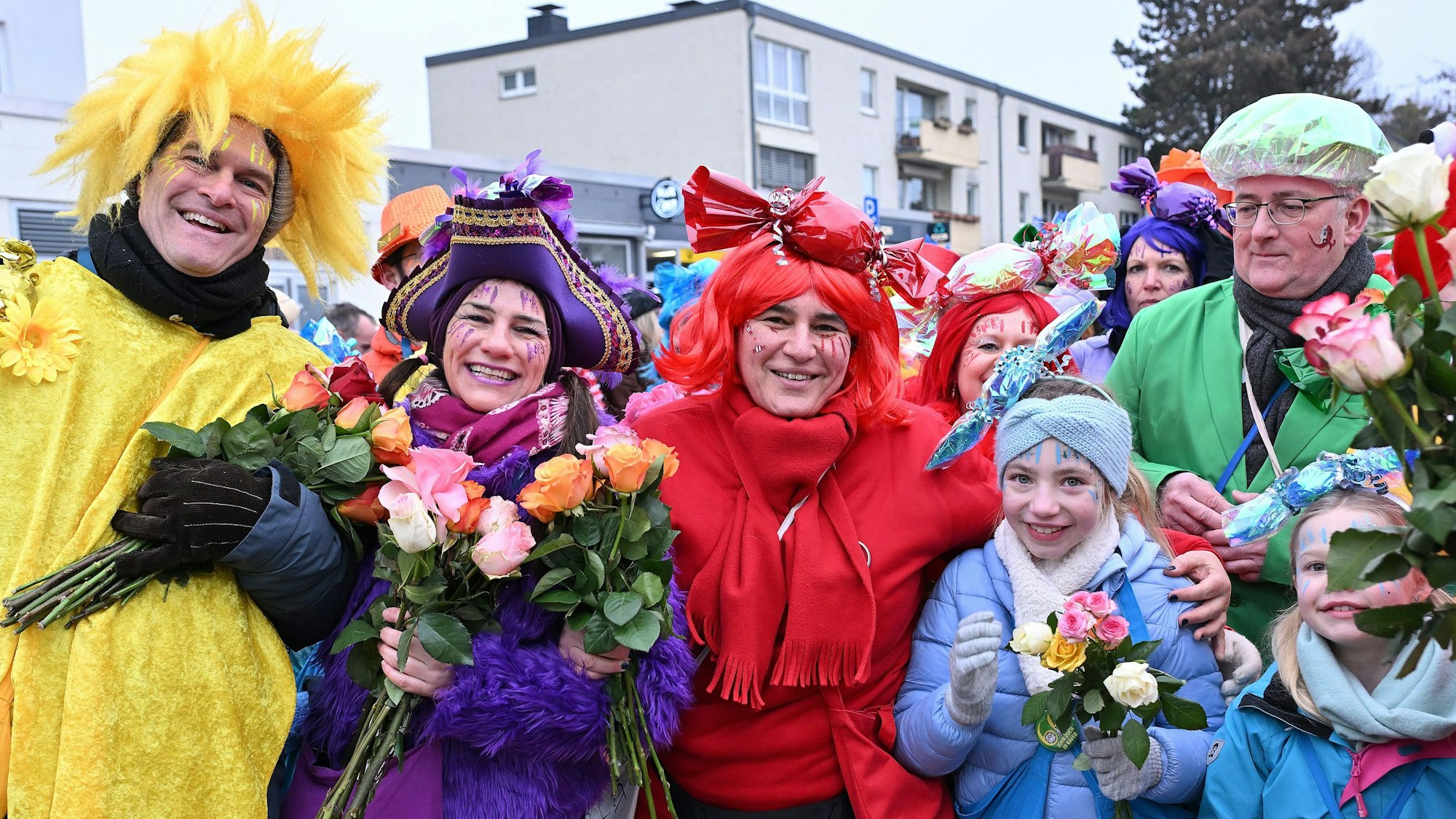 Viele Jecke in bunten Kostümen halten Blumen in den Händen.