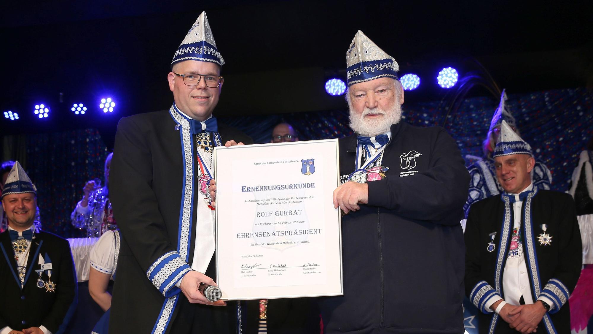 Ein Senatspräsident im Karneval verleiht einem anderen Mann eine Urkunde zum Ehren-Senatspräsidenten.